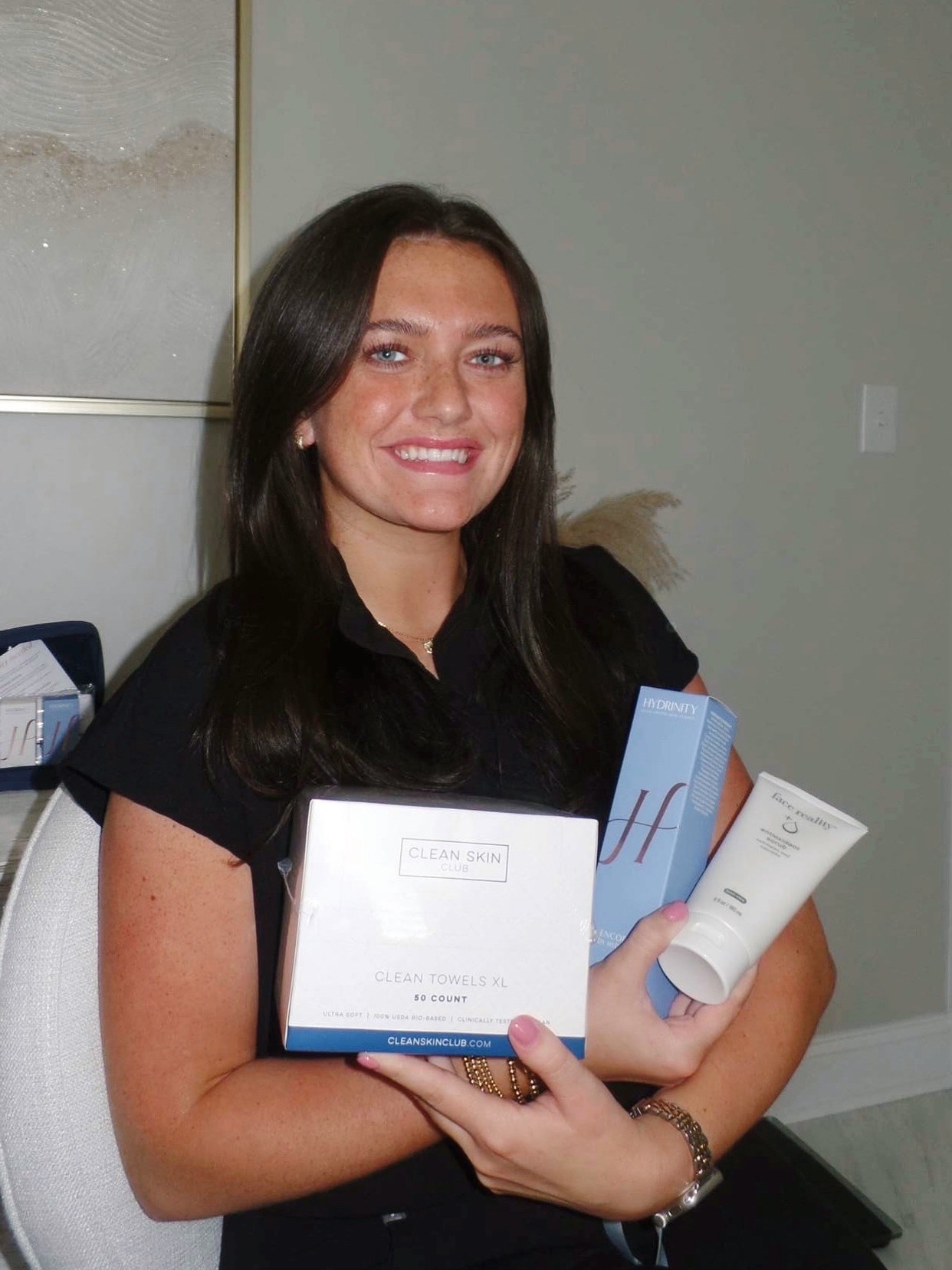 Caroline holding skincare products—Clean Skin Club Clean Towels XL, a Hydrinity box, and a Face Reality cleanser tube.